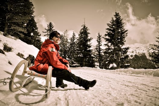 Senior woman siting on sledge sunning in mountain winter snow country with blue sky