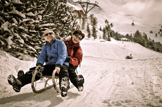 Active senior couple on sledge having fun in mountain snowy country