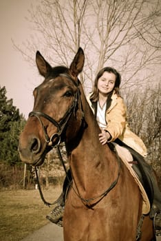 Young woman riding on big brown horse with in sunny day