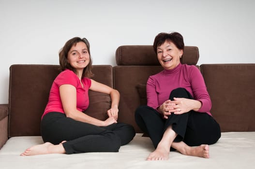 Portrait of happy senior mother and her daughter sitting on sofa at home