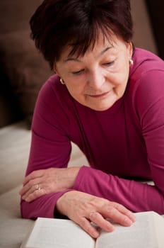 Senior woman reading book at home on sofa