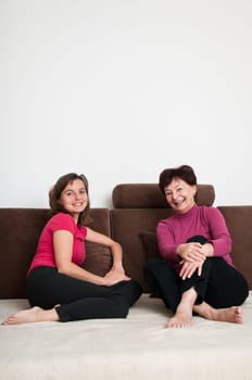 Portrait of happy senior mother and her daughter sitting on sofa at home