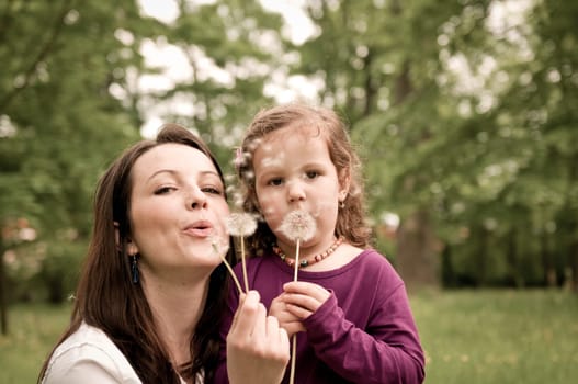 Mother with small daughter blowing to dandelion - lifestyle outdoors scene in park
