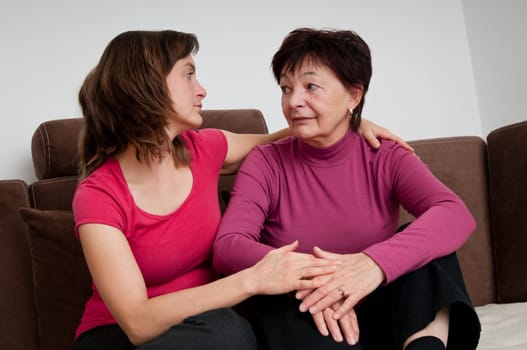 Daughter (young woman) comforts her depressed senior mother at home