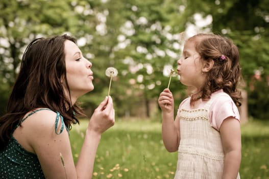 Mother with small daughter blowing to dandelion - lifestyle outdoors scene in park