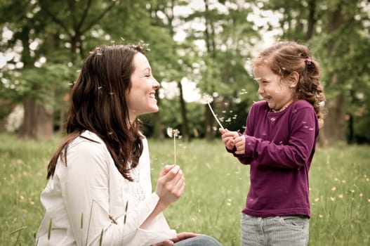Mother with small daughter blowing to dandelion - lifestyle outdoors scene in park