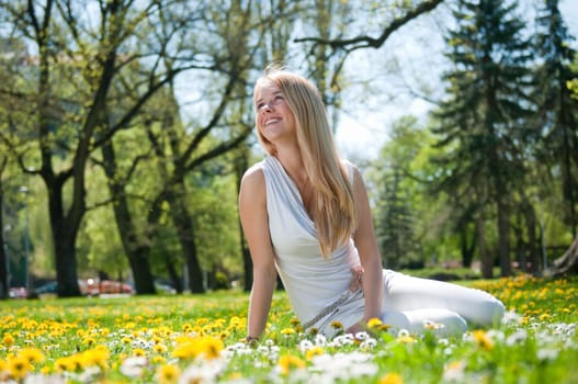 Smiling happy young person (teenager) sitting outdoors in blooming grassfiled and looking away