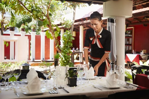 Attractive young woman working as waitress in exclusive restaurant, setting up a table. Waist up, front view