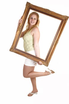 A blond pretty woman in heels and a white shorts and green top, holding a picture frame in front of her, standing for white background.