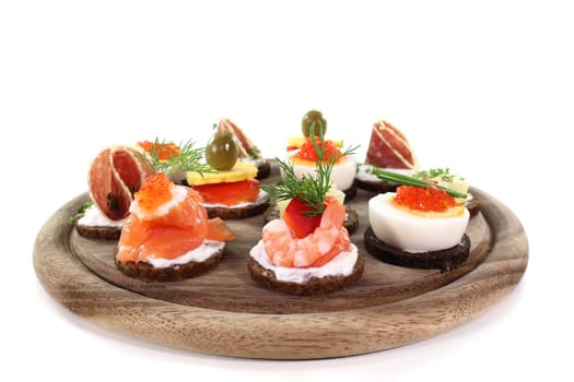 Various canapés on a wooden board against a white background