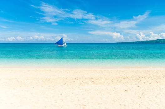 tropical white beach with a sailing boat at the horizon