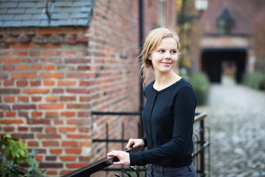 Portrait of a pretty young blond woman standing on a bridge in medieval city quorter and turning back