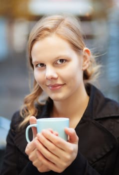 Pretty young woman holding a cup of hot drink outdoors