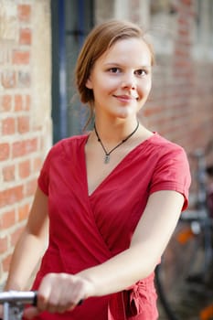 Young blond woman in red dress standing on a street with old bicycle