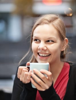 Pretty young woman holding a cup of hot drink in a restaurant terrace outdoors