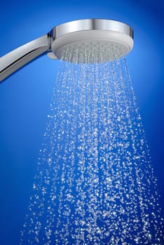 Studio shot of shower head with running water on blue,sharp drops of water