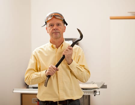 Senior male in a home workshop facing the camera and holding a crowbar