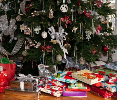 Christmas tree decorated with silver and white ribbons and ornaments with wrapped presents under the tree