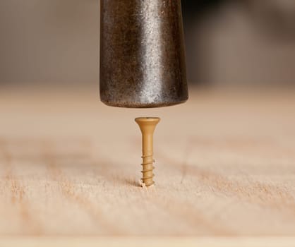 Brown screw being driven into wood by hammer head