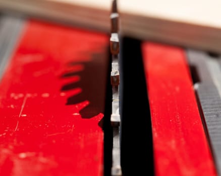 Focus on single carbide tooth of circular saw blade with a piece of plywood out of focus