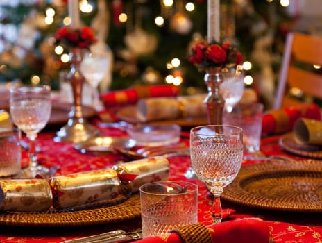 Christmas crackers on table set for Christmas lunch with candles and tree in background
