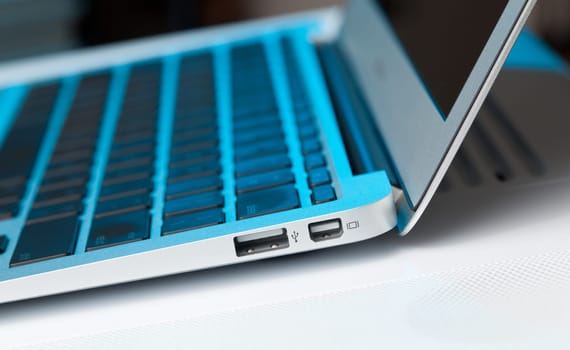 USB socket and mini display port in the side of metal laptop lit with a technology blue tint