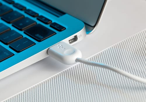 White USB plug inserted into side of metal laptop lit with a technology blue tint