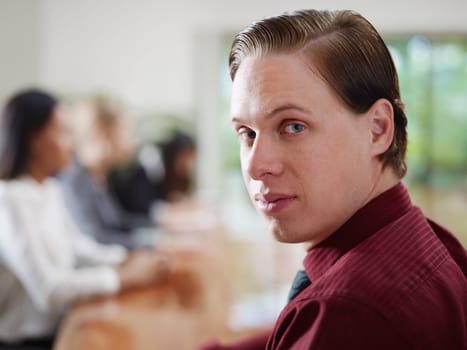 Happy young caucasian businessman smiling at camera during business meeting with colleagues. Rack focus