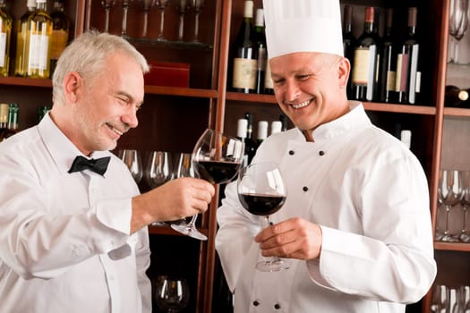 Chef cook and waiter toasting with wine smiling in restaurant