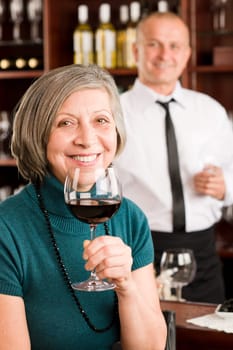 Wine bar senior woman enjoy wine glass in front of bartender