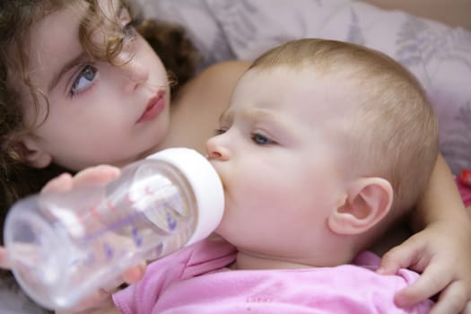 Toddler girl feeding bottle of milk to her baby sister