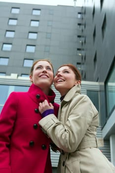 Two happy young women with winter coats, black building background