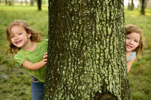 Two twin little sister girls playing on the park tree outdoor