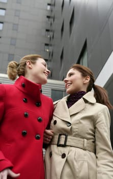 Two happy young women with winter coats, black building background