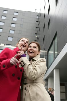 Two happy young women with winter coats, black building background