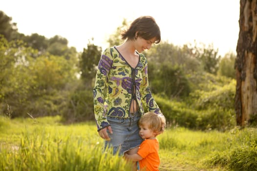 blond toddler son hug his mother in green outdoor