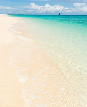 tropical white beach with a sailing boat at the horizon