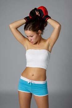 Sporty girl in red fighting gloves on a gray background.