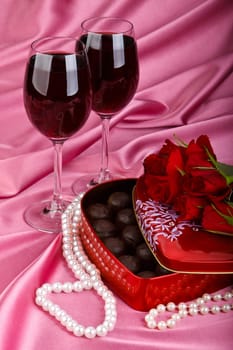 Heart-shaped red box with sweets, two glasses of red wine and bunch of flowers. Valentine&#039 s day card.