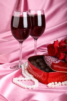 Heart-shaped red box with sweets, two glasses of red wine and bunch of flowers. Valentine&#039 s day card.