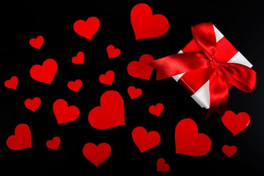 Gift box and red hearts on a black background. Valentine&#039 s day card.