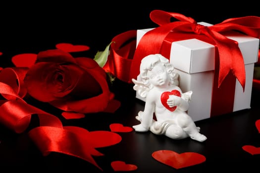 Gift box, cupid, red hearts and rose on a black background. Valentine&#039 s day card.