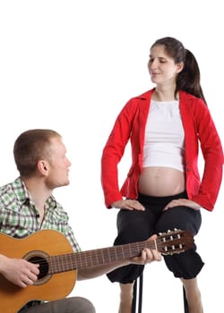 The young husband plays a guitar for the pregnant wife and the future child on a white background.