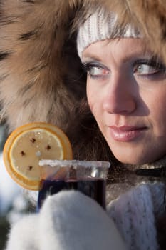 The beautiful girl drinks mulled wine in winter wood.
