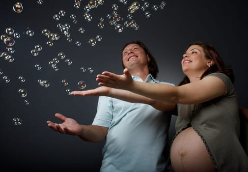 Happy beautiful pregnant woman and her husband catches soap bubbles