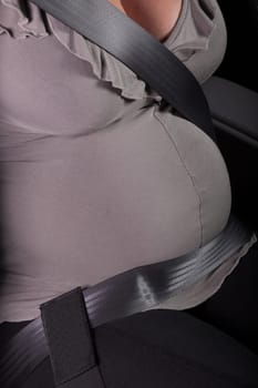The pregnant woman fastened by a seat belt sits in the car.