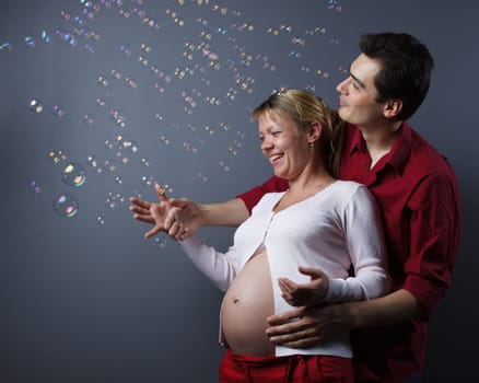 Happy beautiful pregnant woman and her husband catches soap bubbles