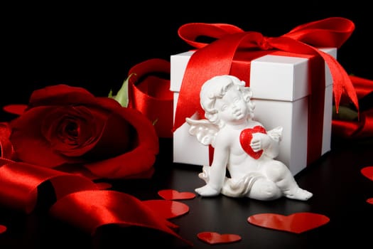 Gift box, cupid, red hearts and rose on a black background. Valentine&#039 s day card.