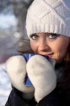 The beautiful girl with a cup of a hot drink in winter wood.