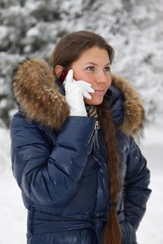 The beautiful girl with a mobile phone in winter park.